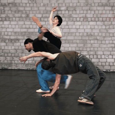 Drei Tänzer*innen stehen eng beieinander und performanen dynamisch in verschiedenen Tanzstilen